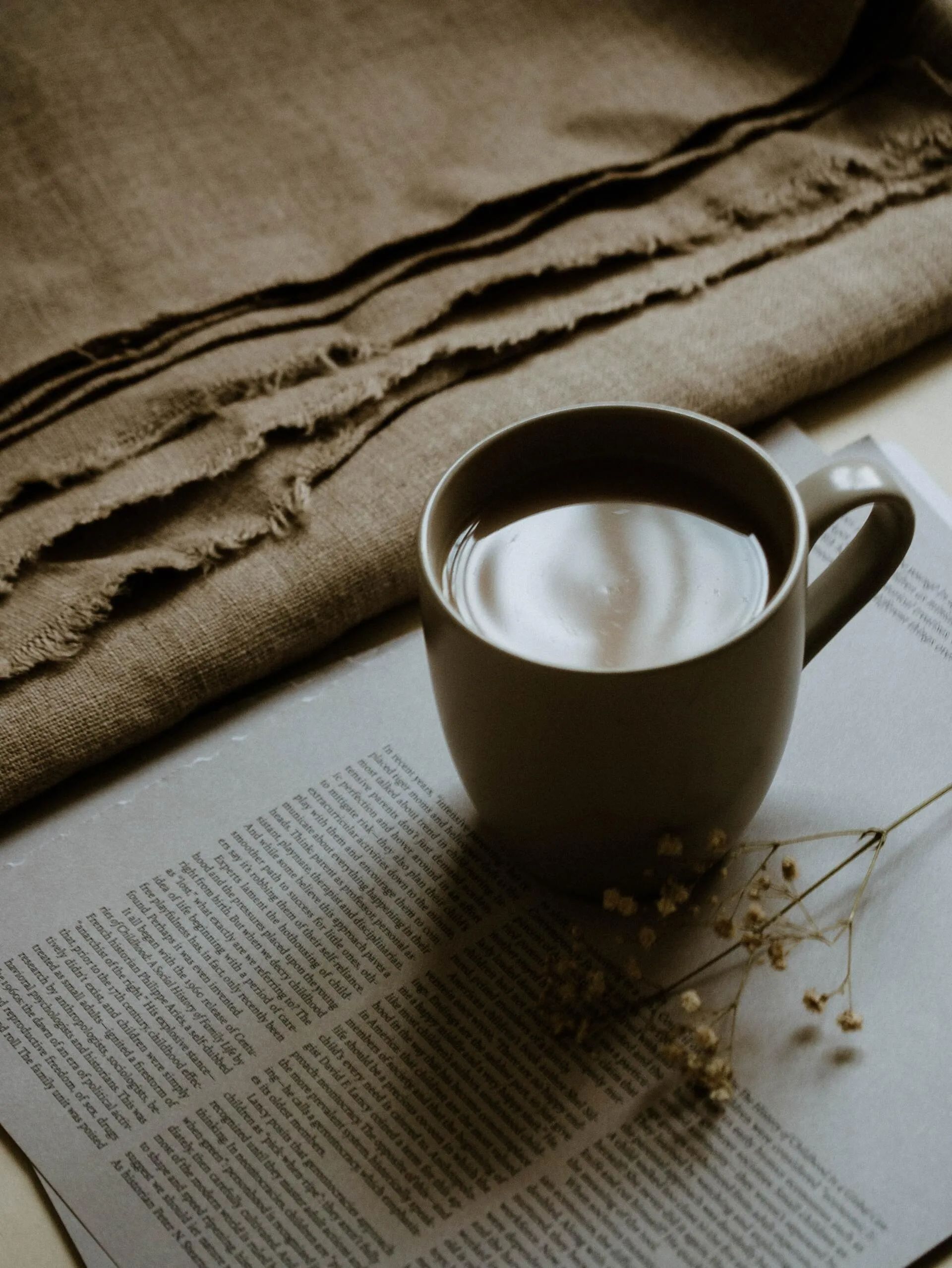 A mug of coffee sits on a book next to a burlap cloth. The scene is warm-toned and cozy.