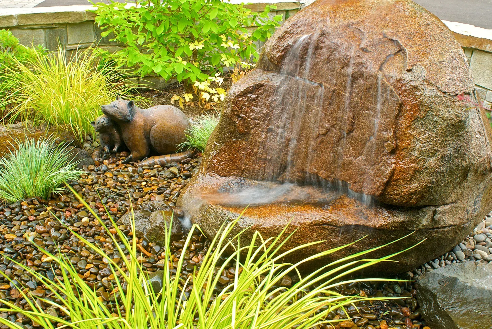 A brown rock fountain with water cascading down, surrounded by greenery and a marmot statue.