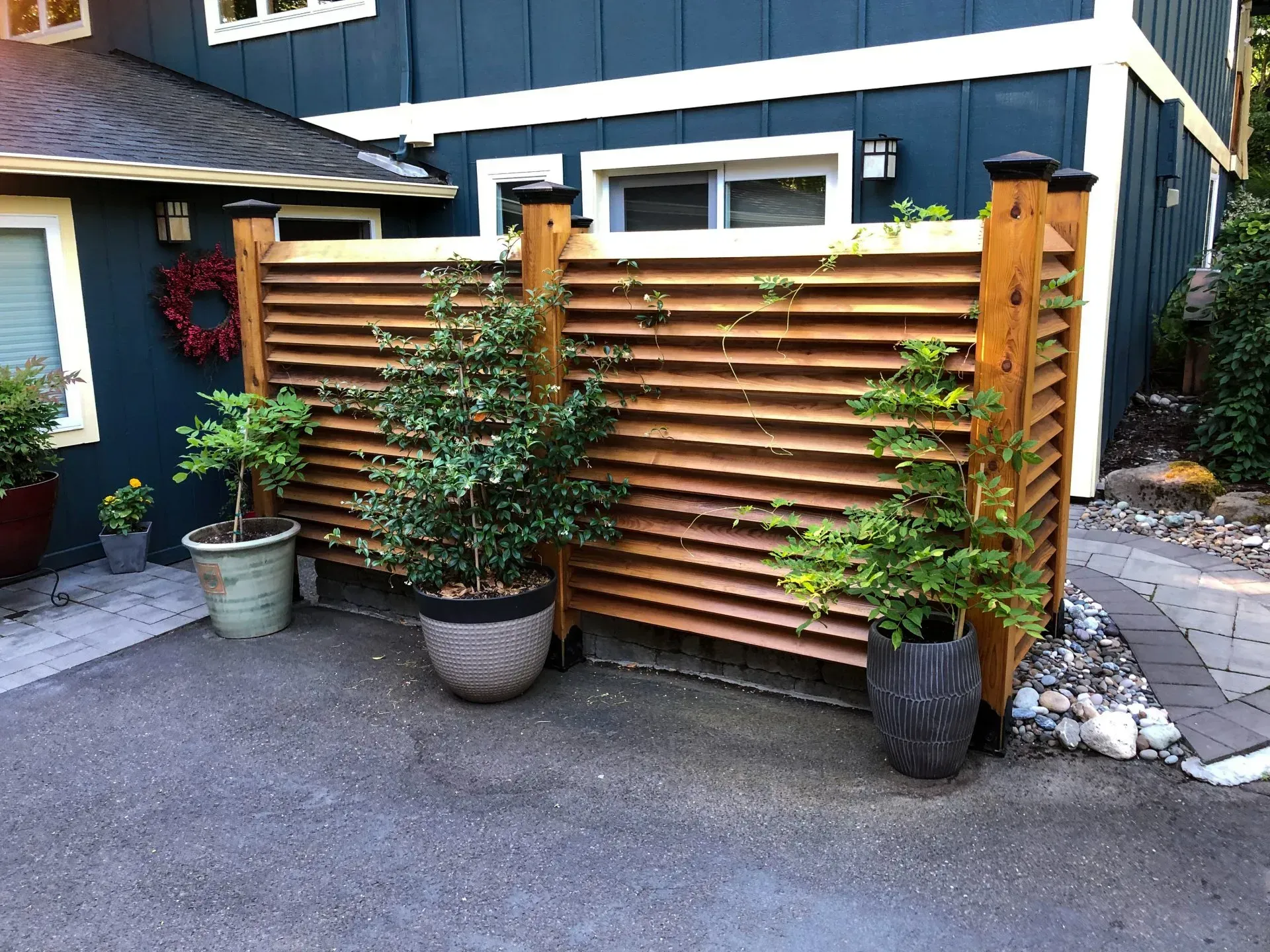 A wooden slat fence with potted plants in front of a blue house.