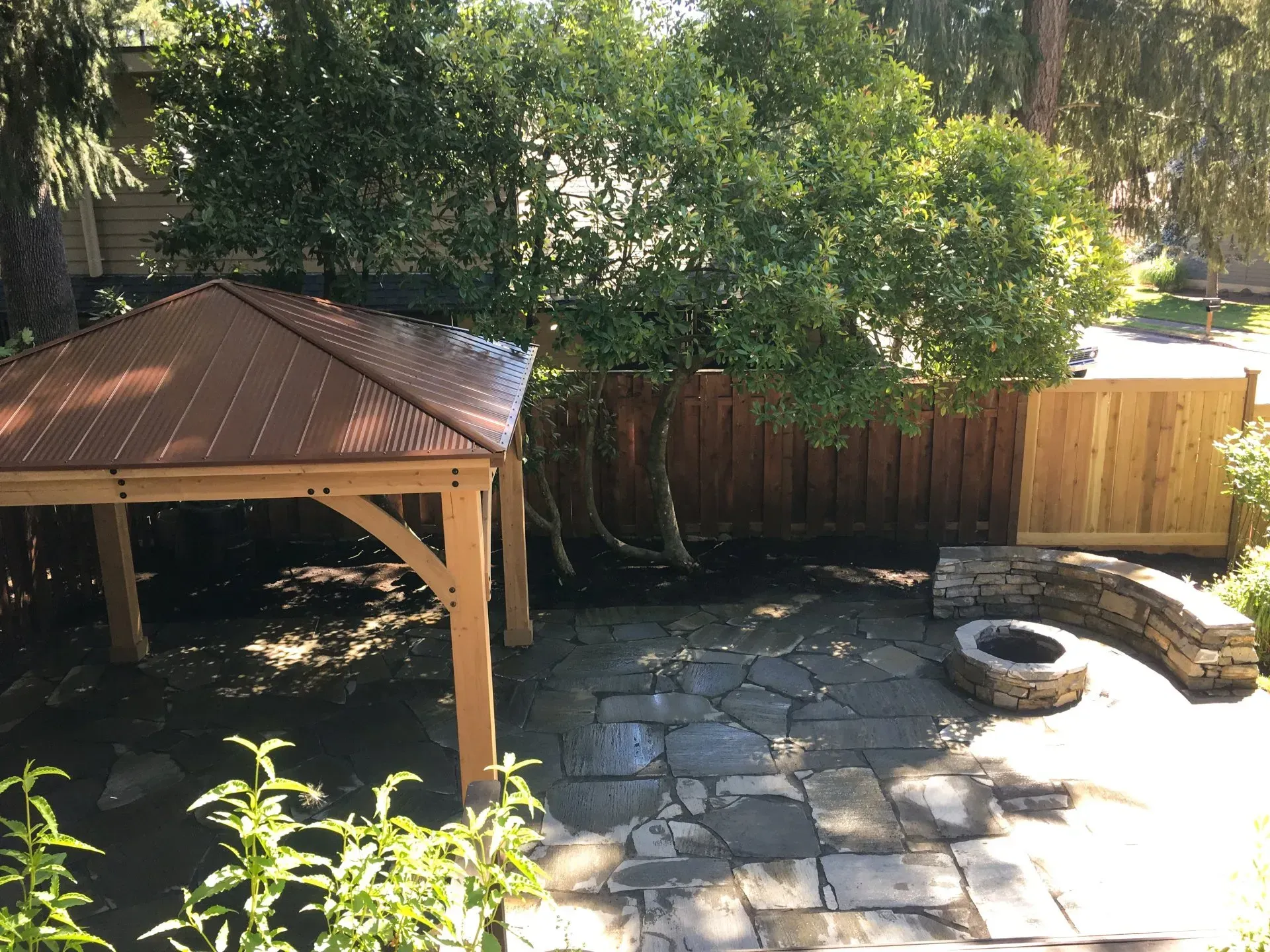 Outdoor patio with gazebo, stone path, fire pit, and wooden fence. 