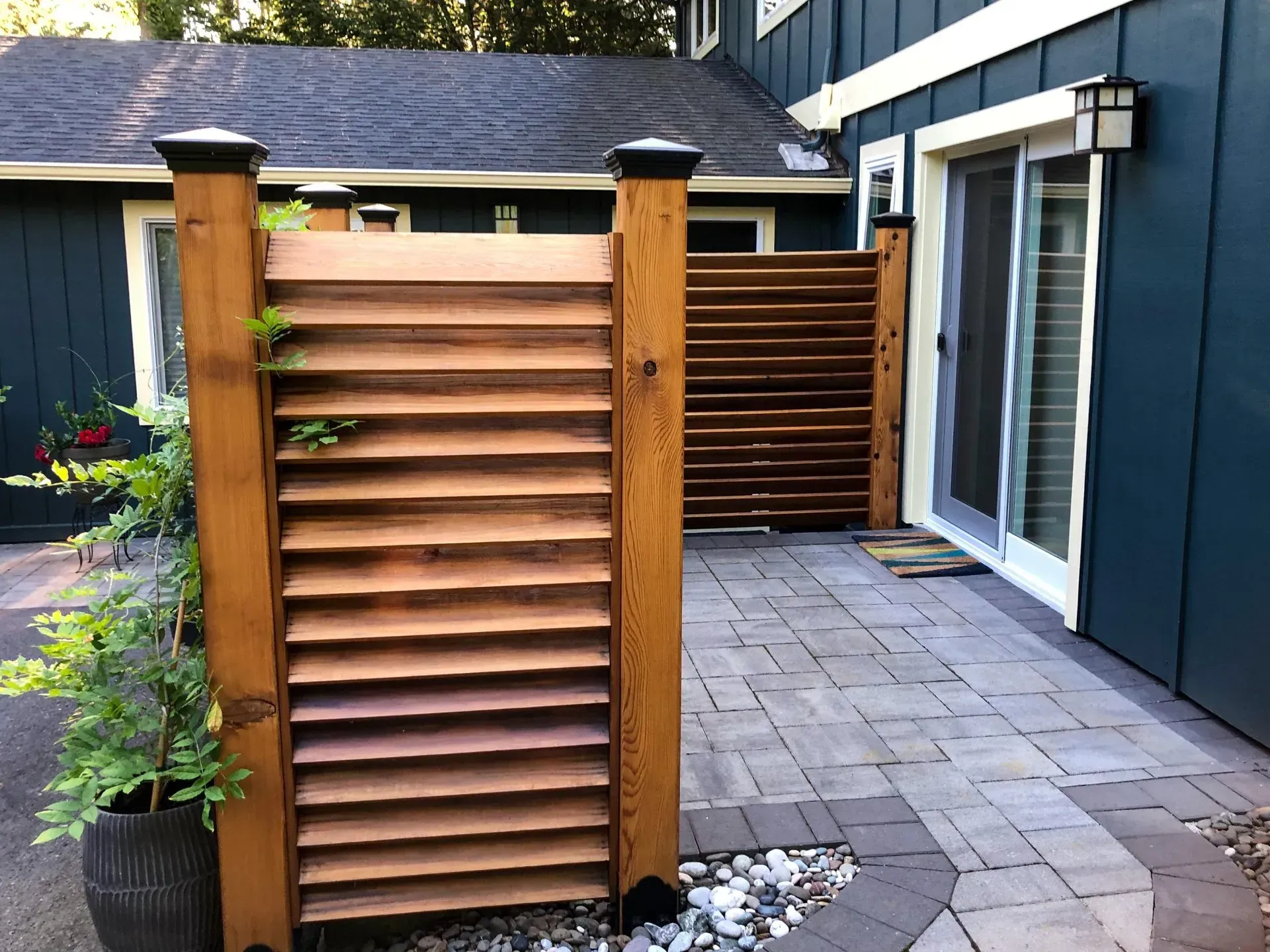 Wooden privacy screens on a stone patio next to a blue house with a sliding glass door.