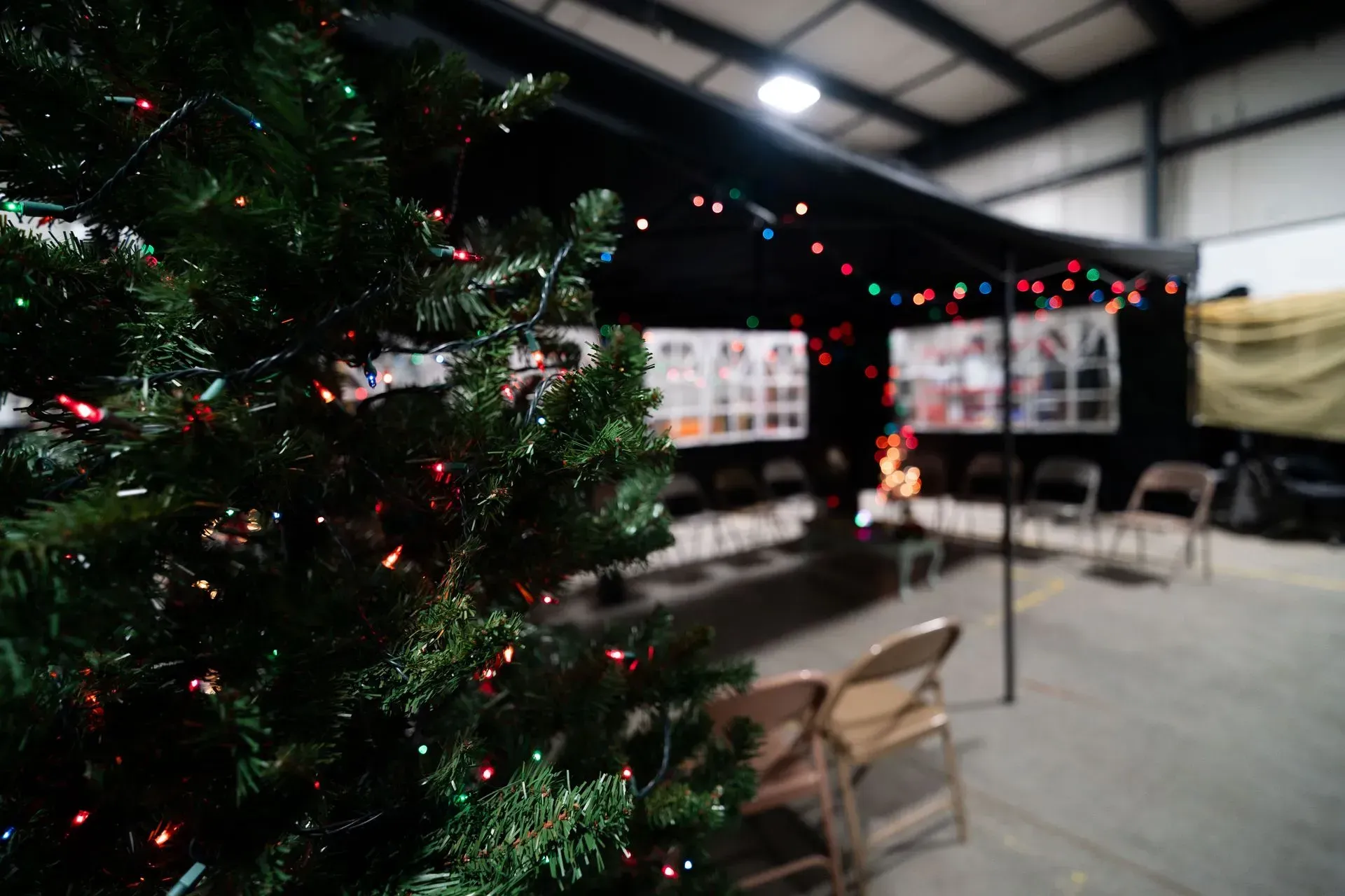 Christmas tree with colorful lights in front of a tent decorated with lights and photos in an industrial building.