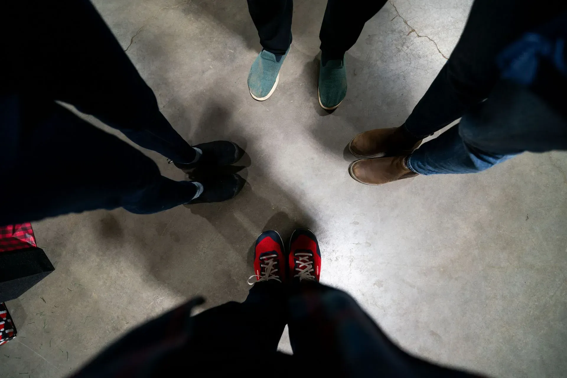 People stand in a circle, their feet touching.  Shoes include red, brown, green, and black.  View is from above.