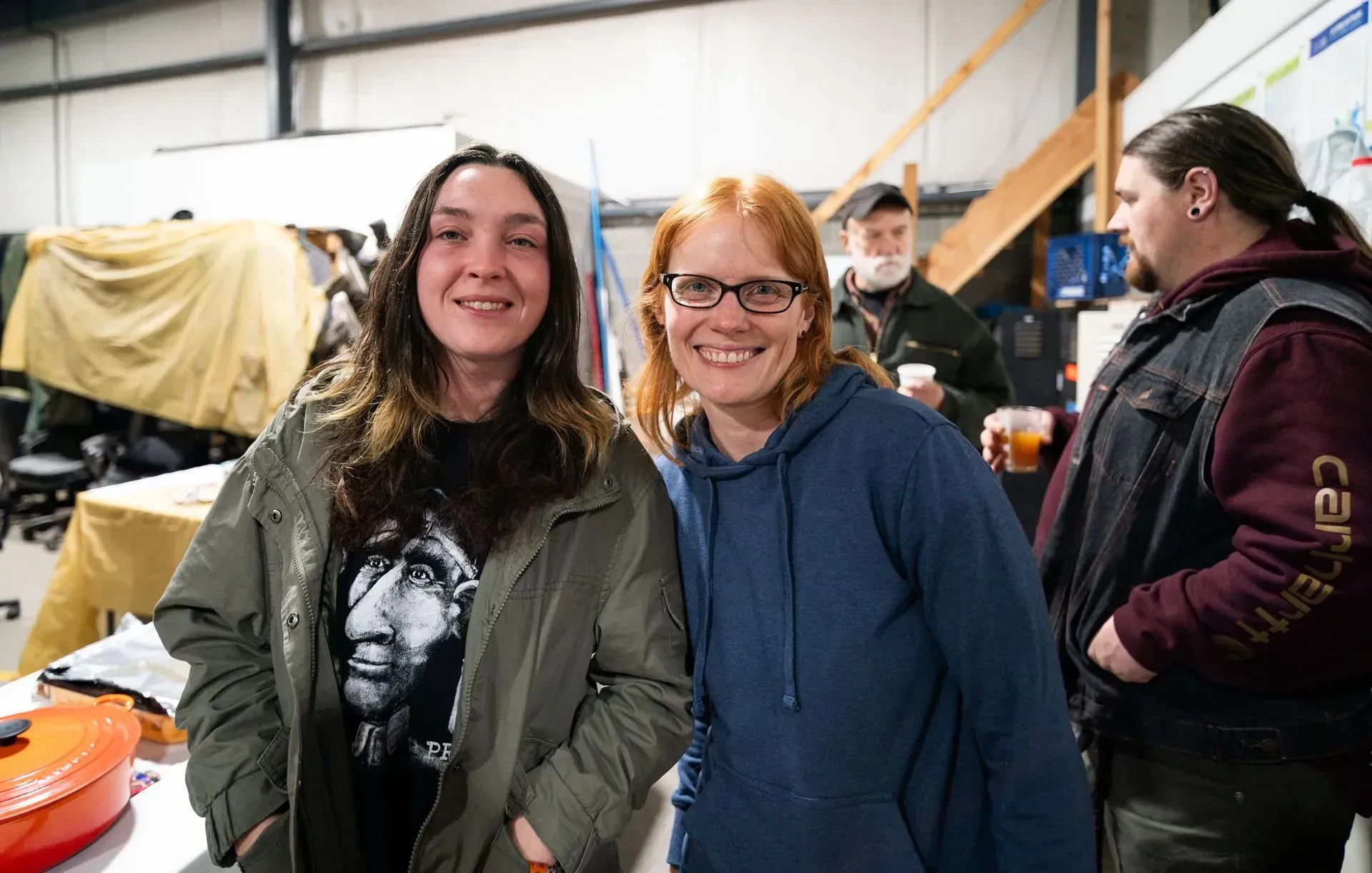 Two smiling women pose indoors, one with long hair and a printed shirt.