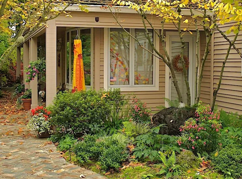 A small tan house with a lush garden. The entrance has a hanging orange decoration and a welcoming wreath.
