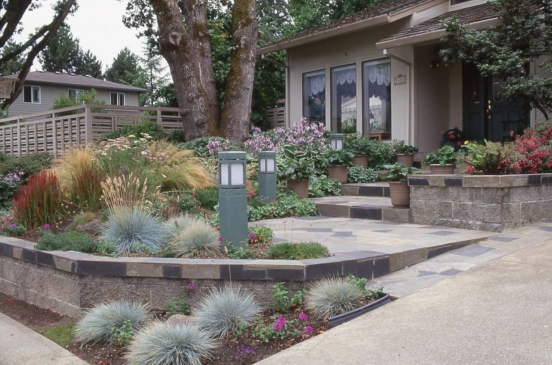 A house with a garden, including stone steps, plants, and two gray light posts.
