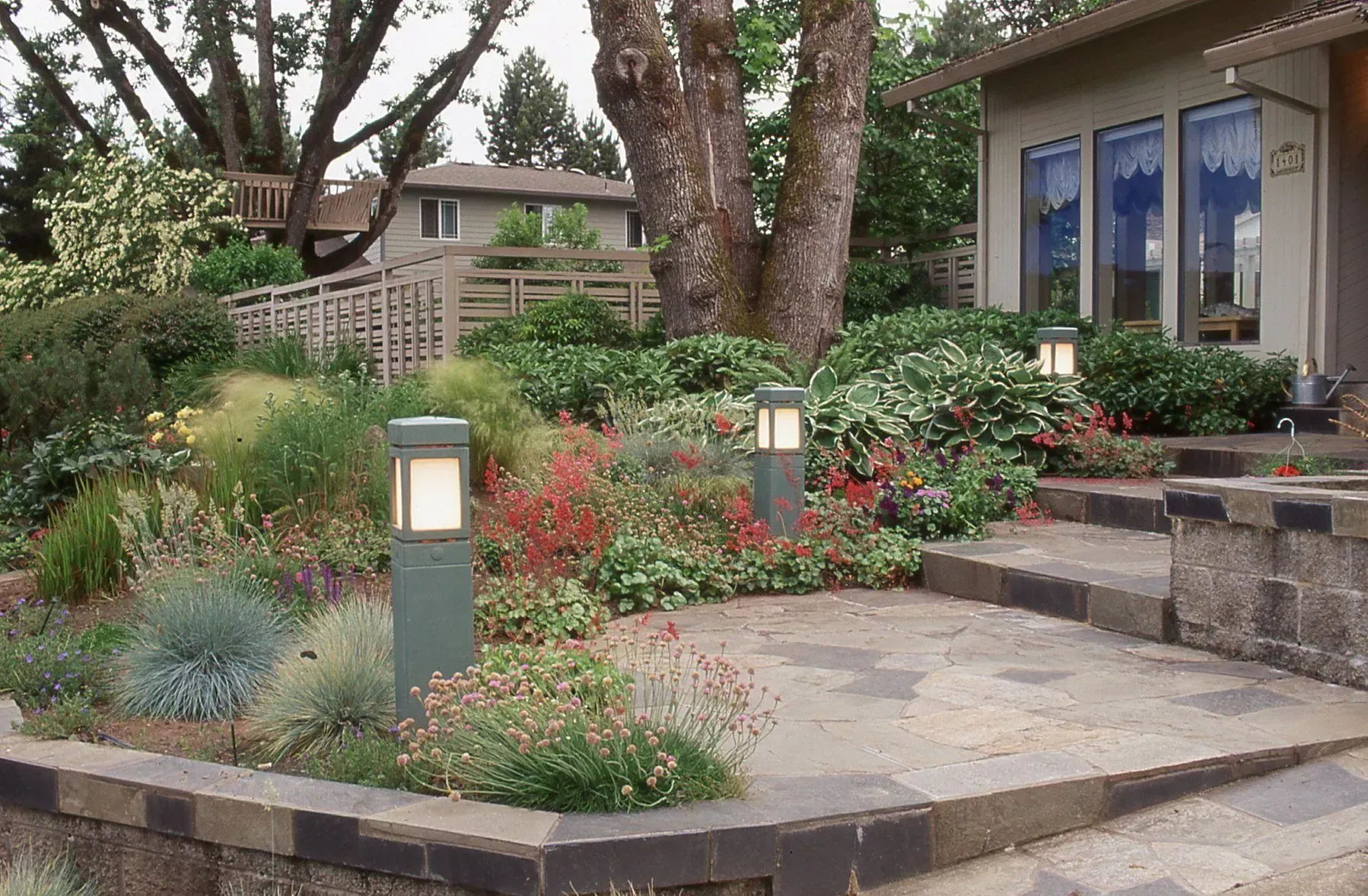 Stone patio with landscaping and three rectangular outdoor lights in front of a house.