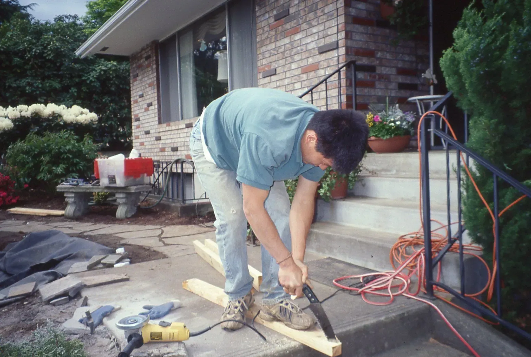 A person sawing wood on the steps of a house, likely part of a construction or renovation project outdoors.