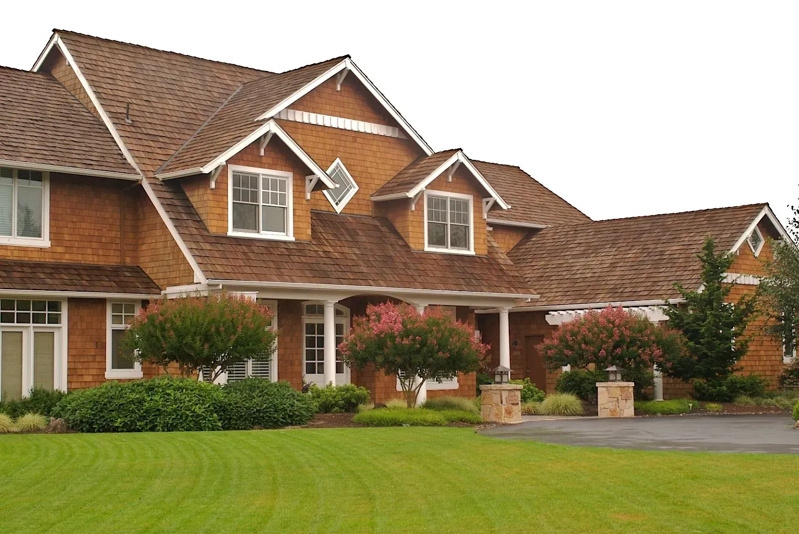 Two-story brick house with brown shingled roof, white trim, and a green lawn. 