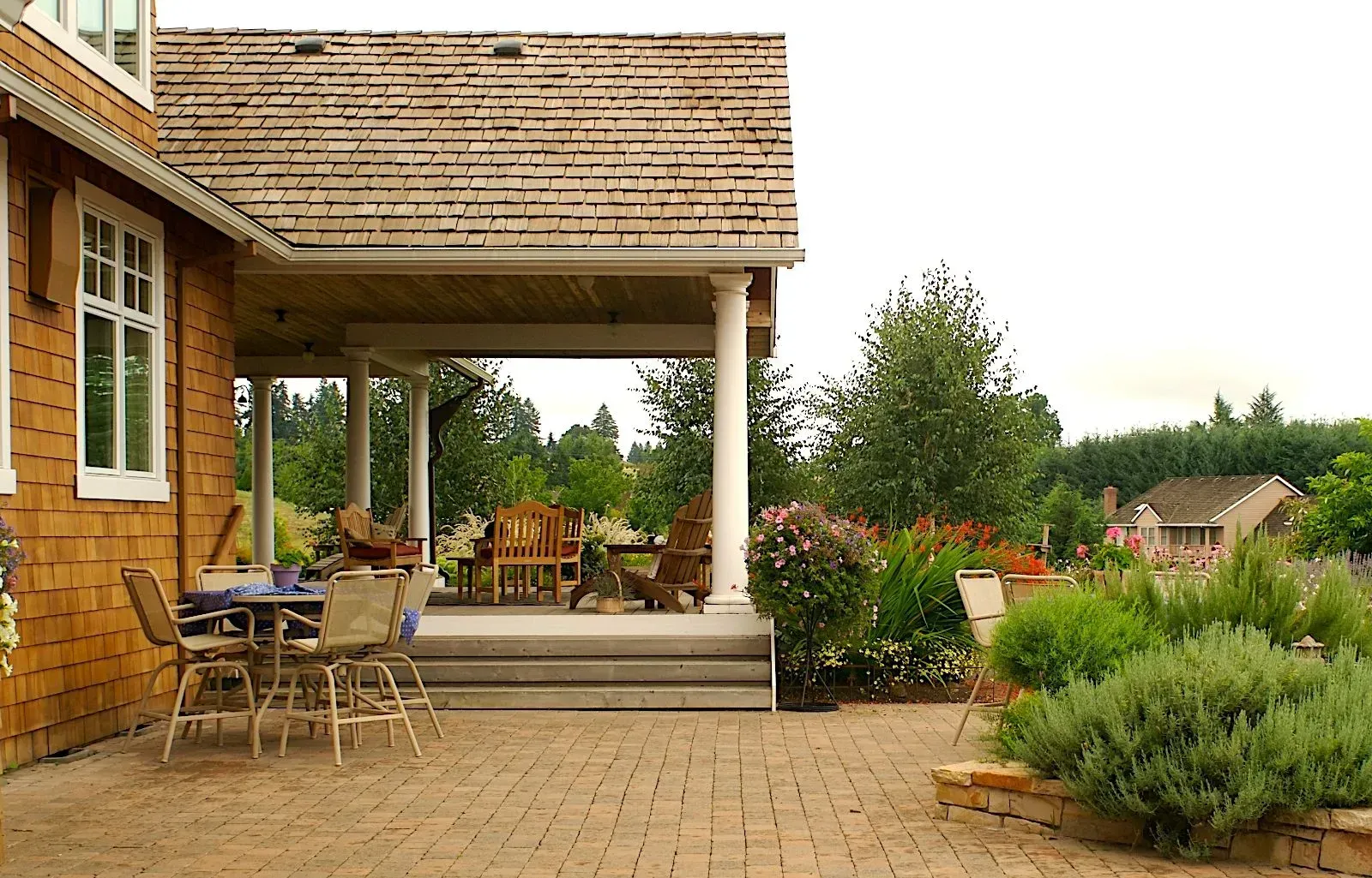 A brick patio with a wooden porch supported by white columns, outdoor furniture, and a garden.