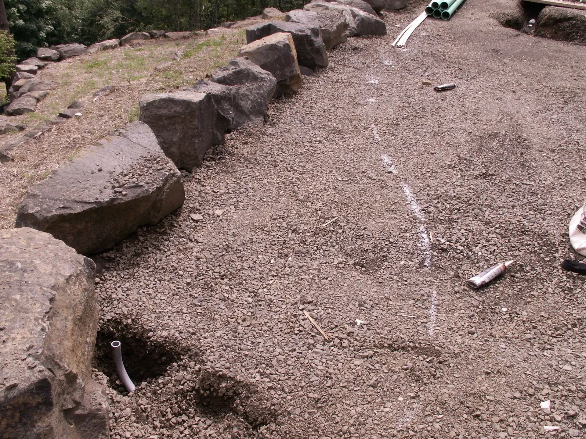 A gravel-covered landscape with large rocks forming a border. Electrical conduits emerge from the ground.