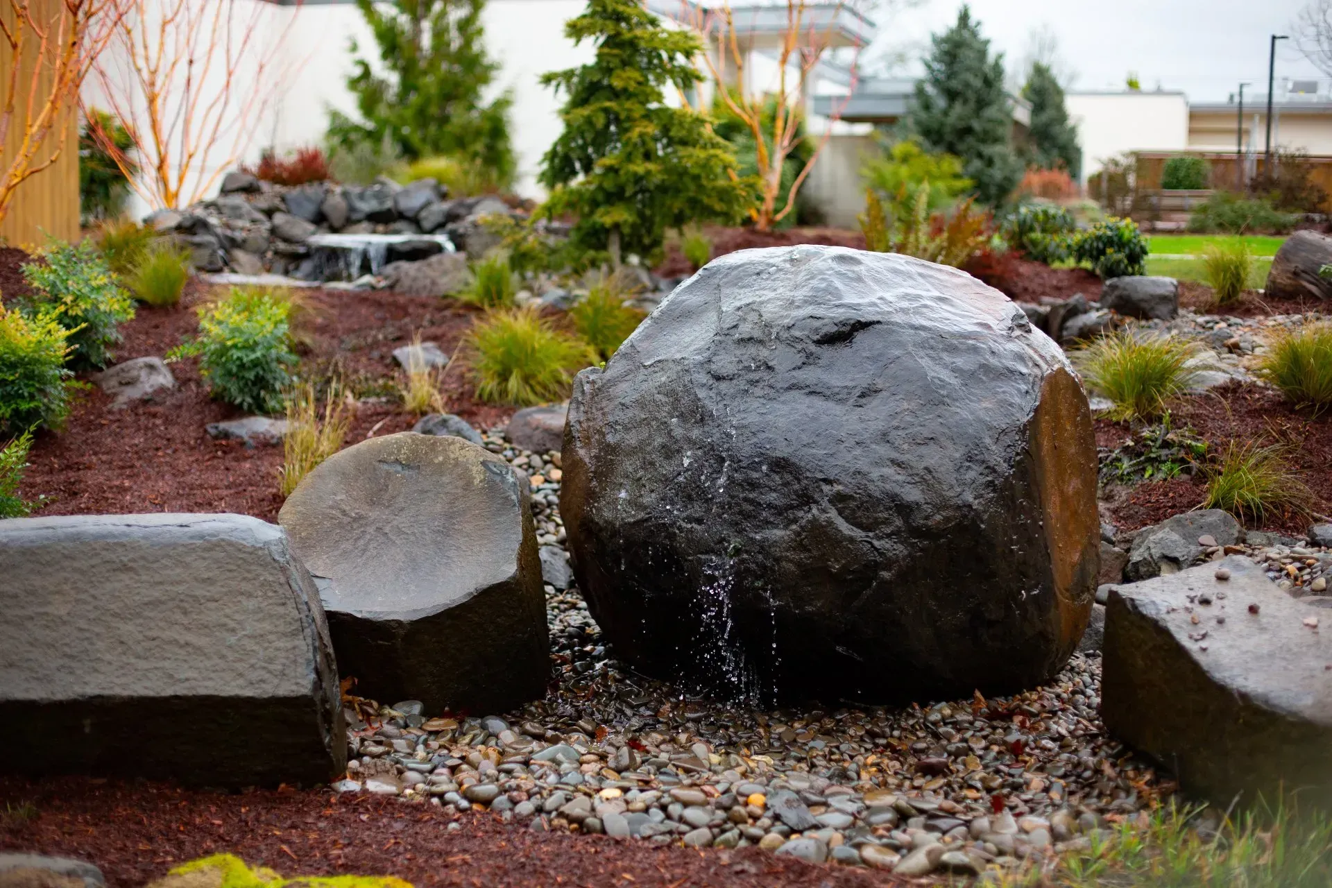 Water fountain feature in a garden with large, dark, rounded rocks.