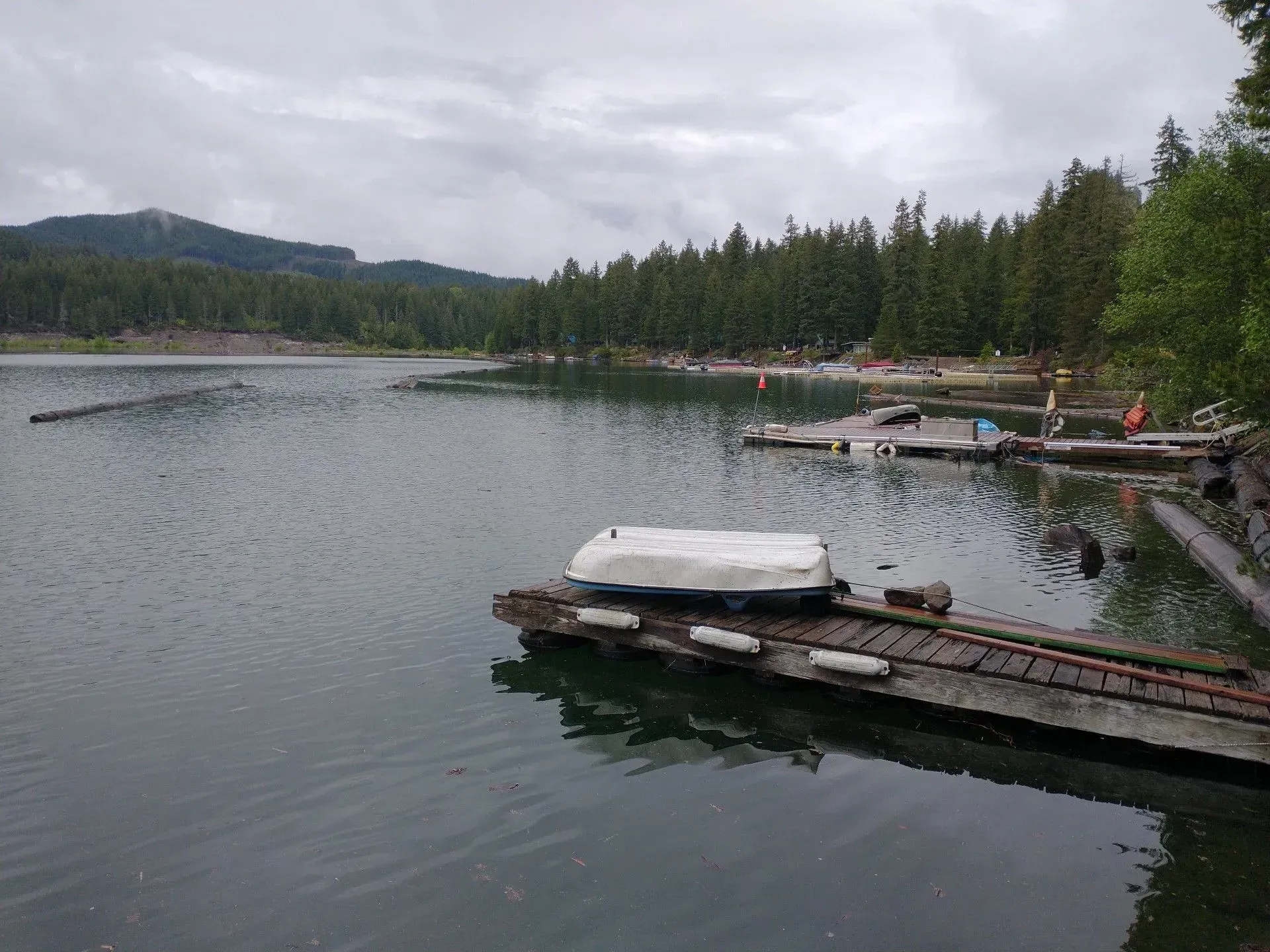 A calm lake with docks and a boat covered with a tarp. Trees line the far shore under a cloudy sky.