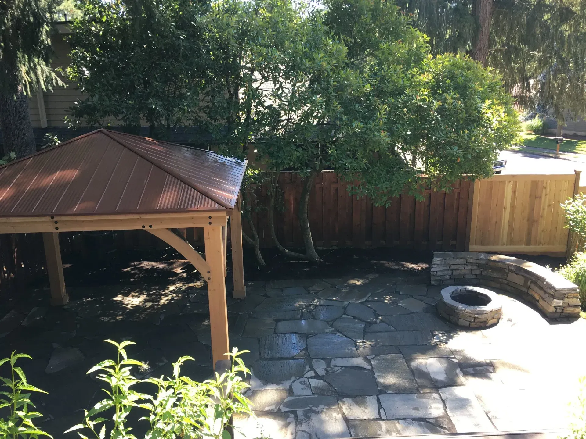 Outdoor patio with a wooden gazebo, flagstone floor, fire pit, and wooden fence.