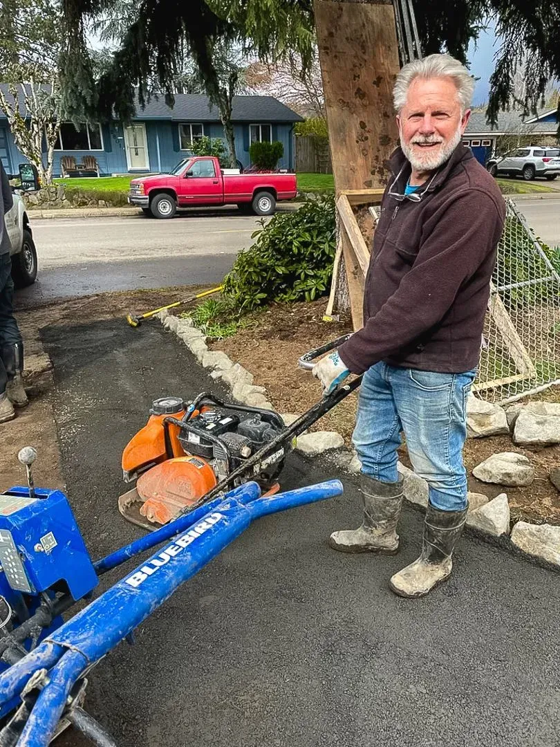 Man using a plate compactor on a newly paved driveway.