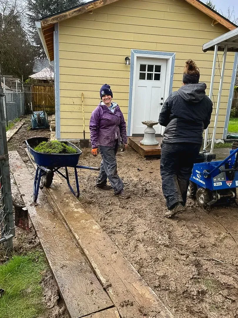 Two people gardening near a yellow shed.