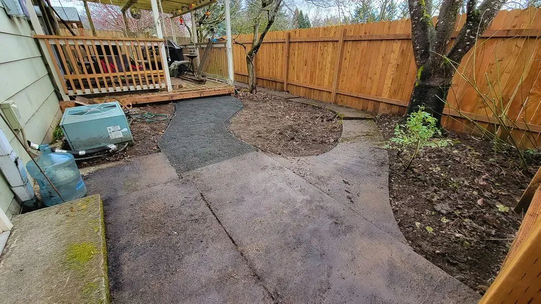A small backyard with a concrete patio and gravel path. A wooden fence and a small deck are visible.