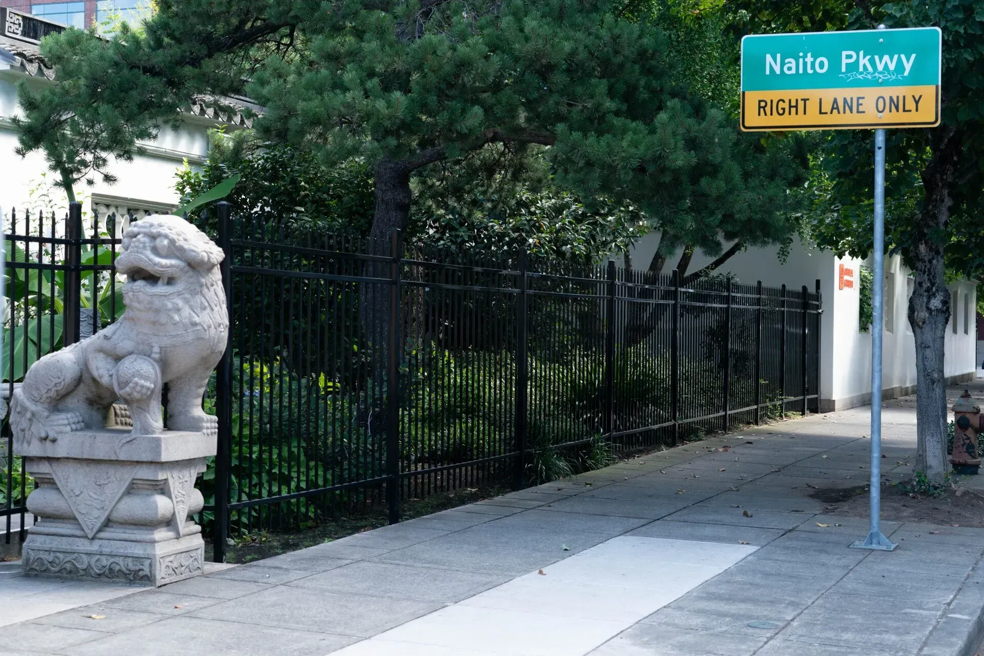 A stone lion statue sits on a pedestal next to a sidewalk, with a sign for Naito Pkwy: Right Lane Only.