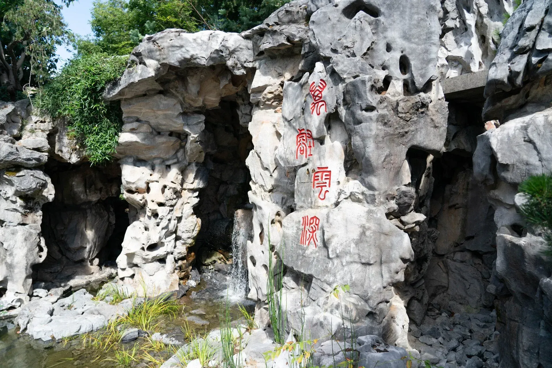 A rock formation with Chinese characters carved in red, overhanging a small pool of water with a waterfall.