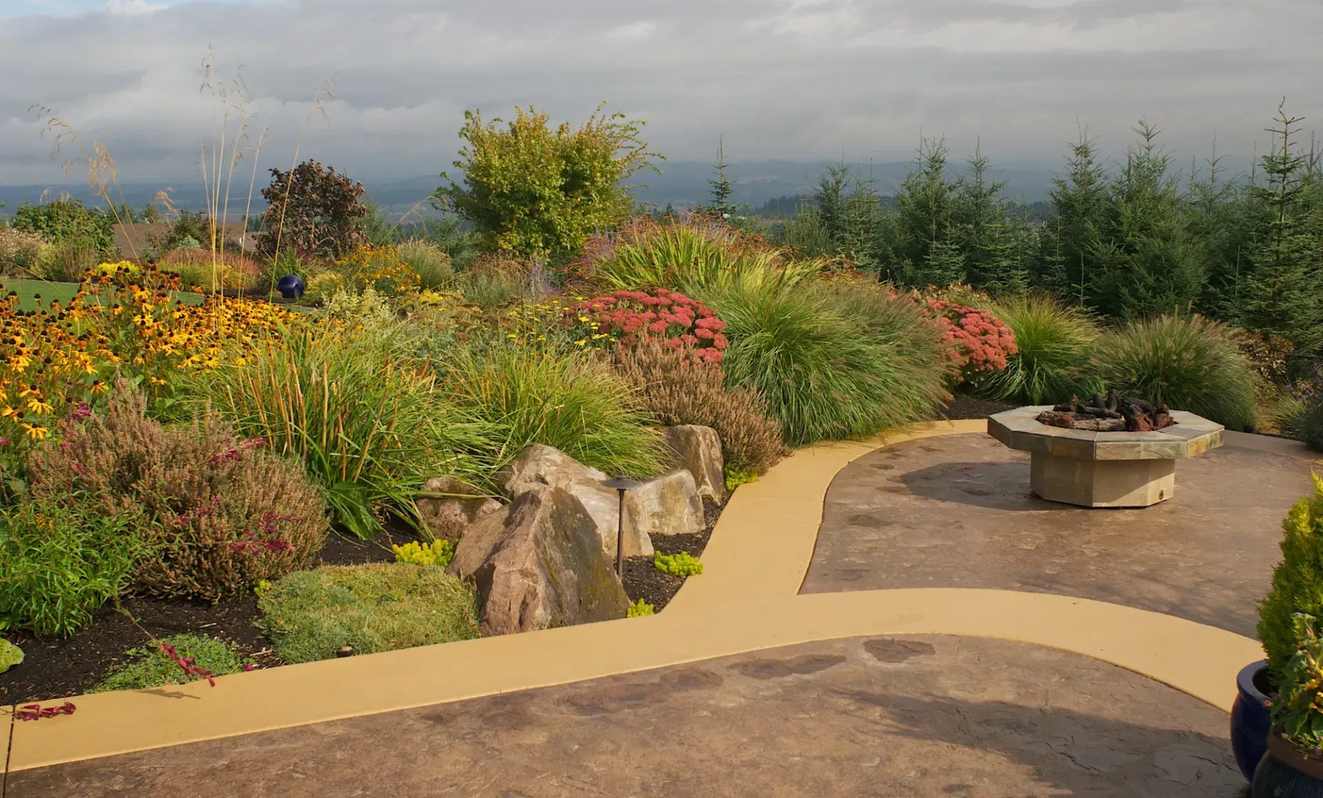 A landscaped garden with a winding path, large rocks, and a fire pit.