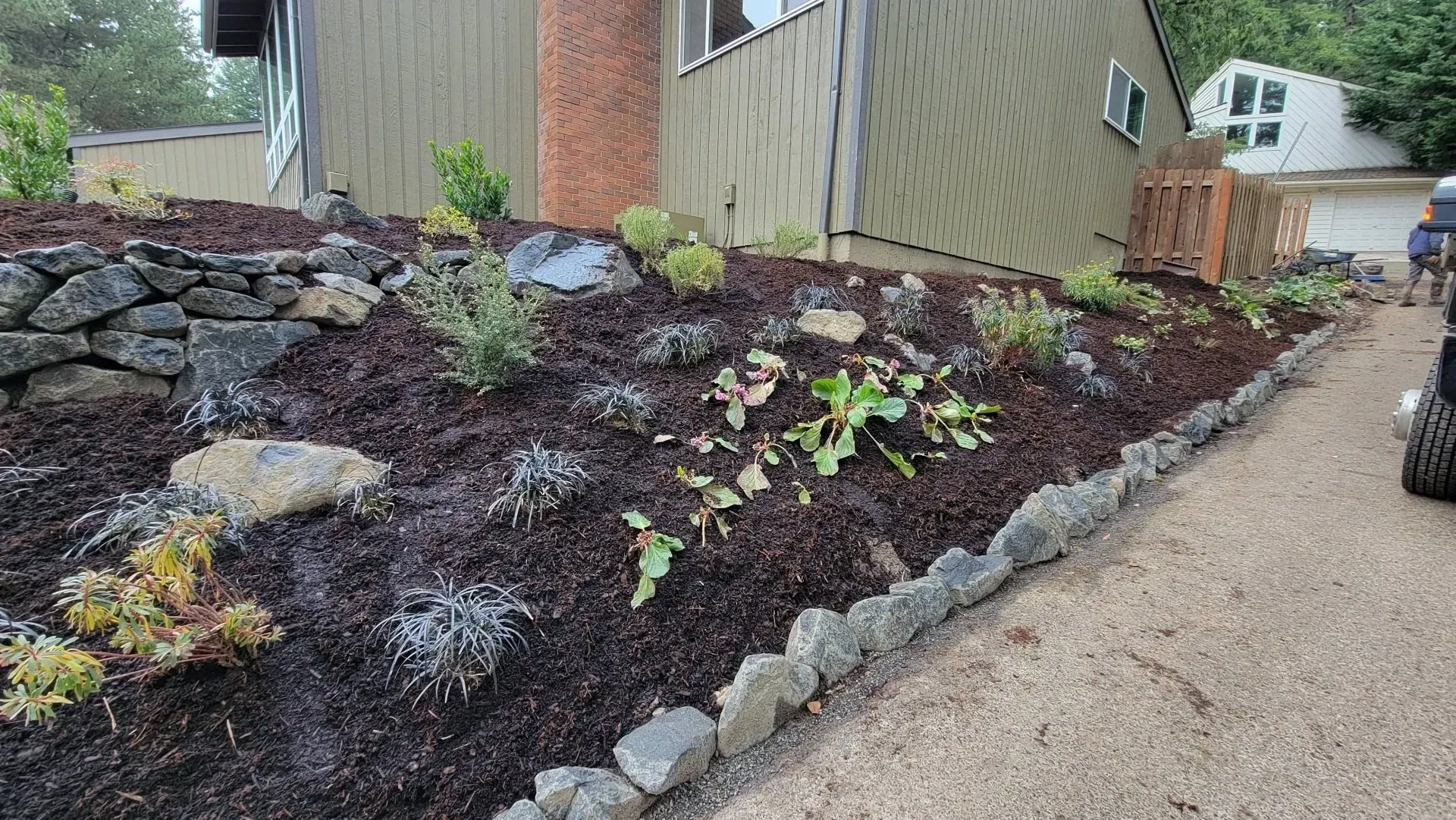 A landscaped front yard with a stone border, dark mulch, and various plants next to a house.