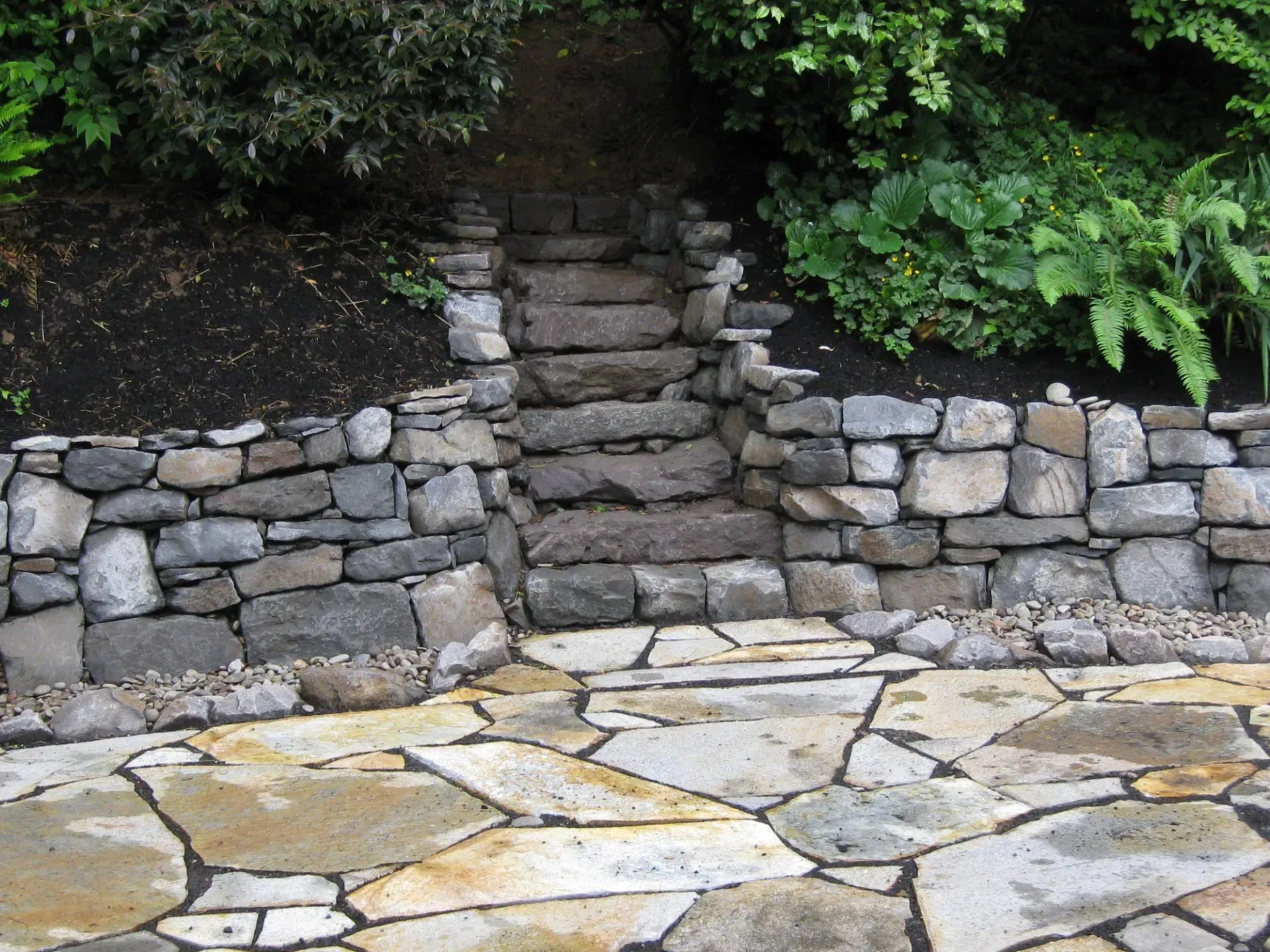 Stone steps leading up a hillside, flanked by stone walls and a flagstone pathway. 