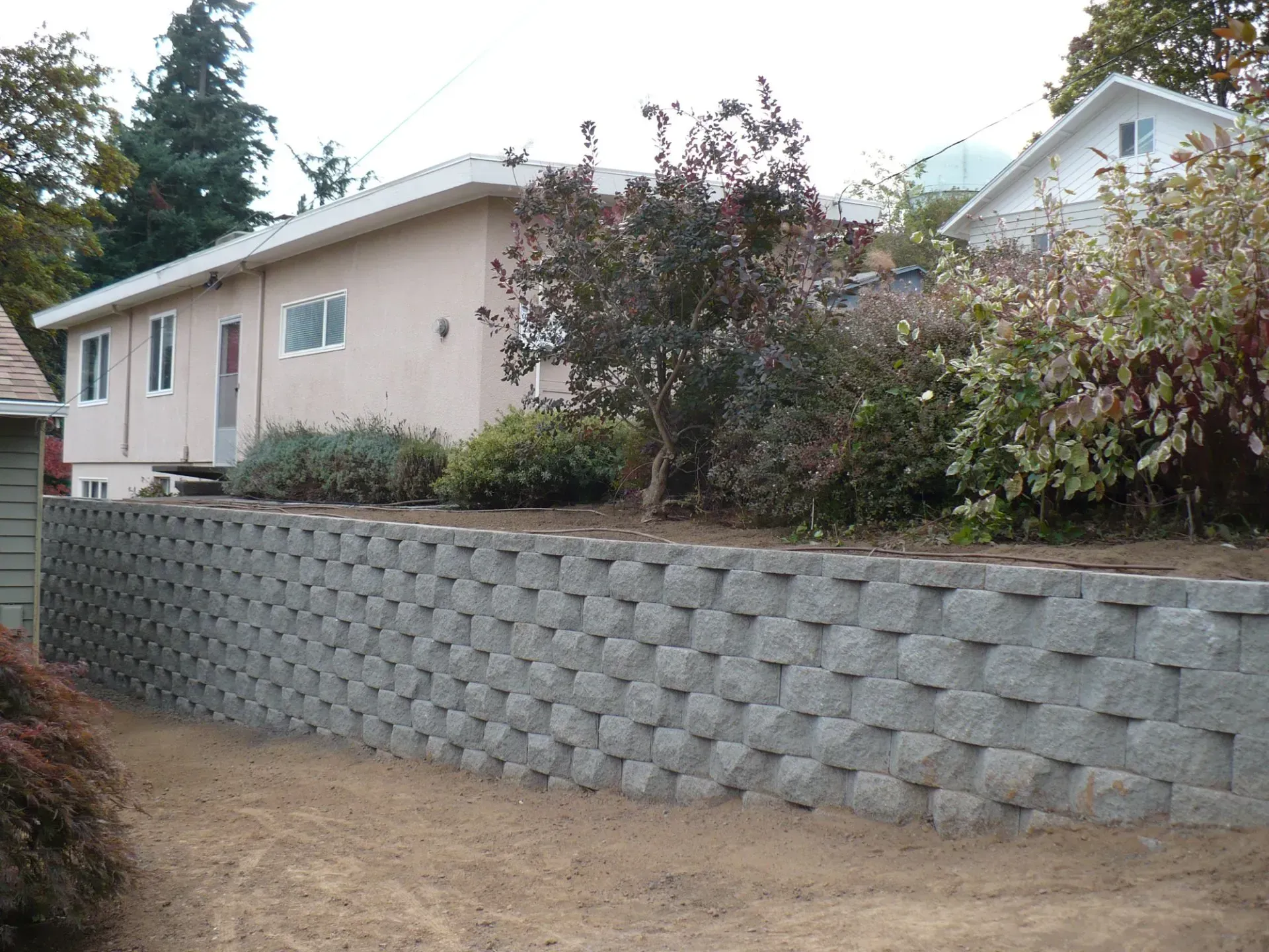 Gray stone retaining wall in front of a light pink house with landscaping.