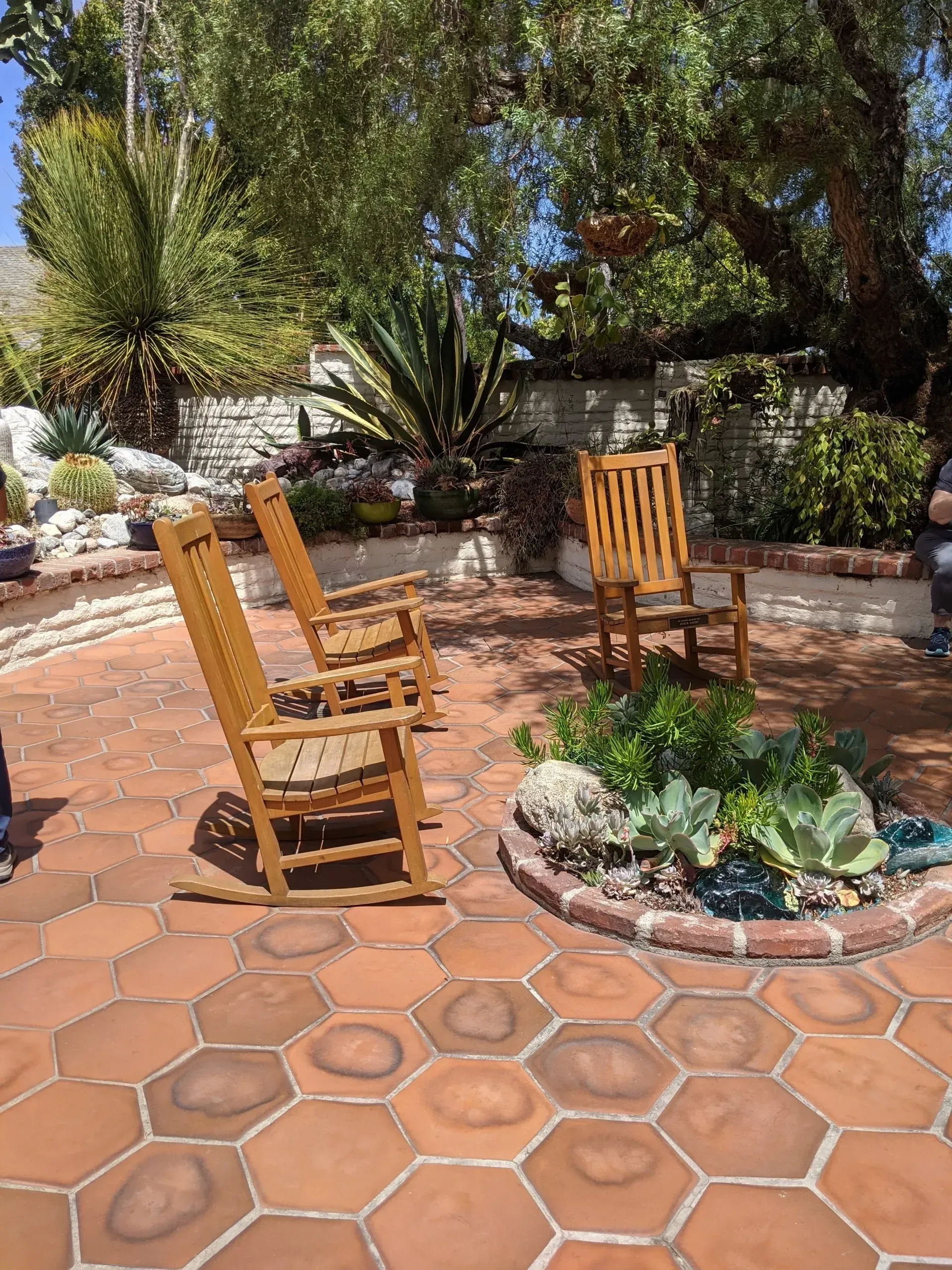 Three wooden rocking chairs on a hexagonal terracotta patio.