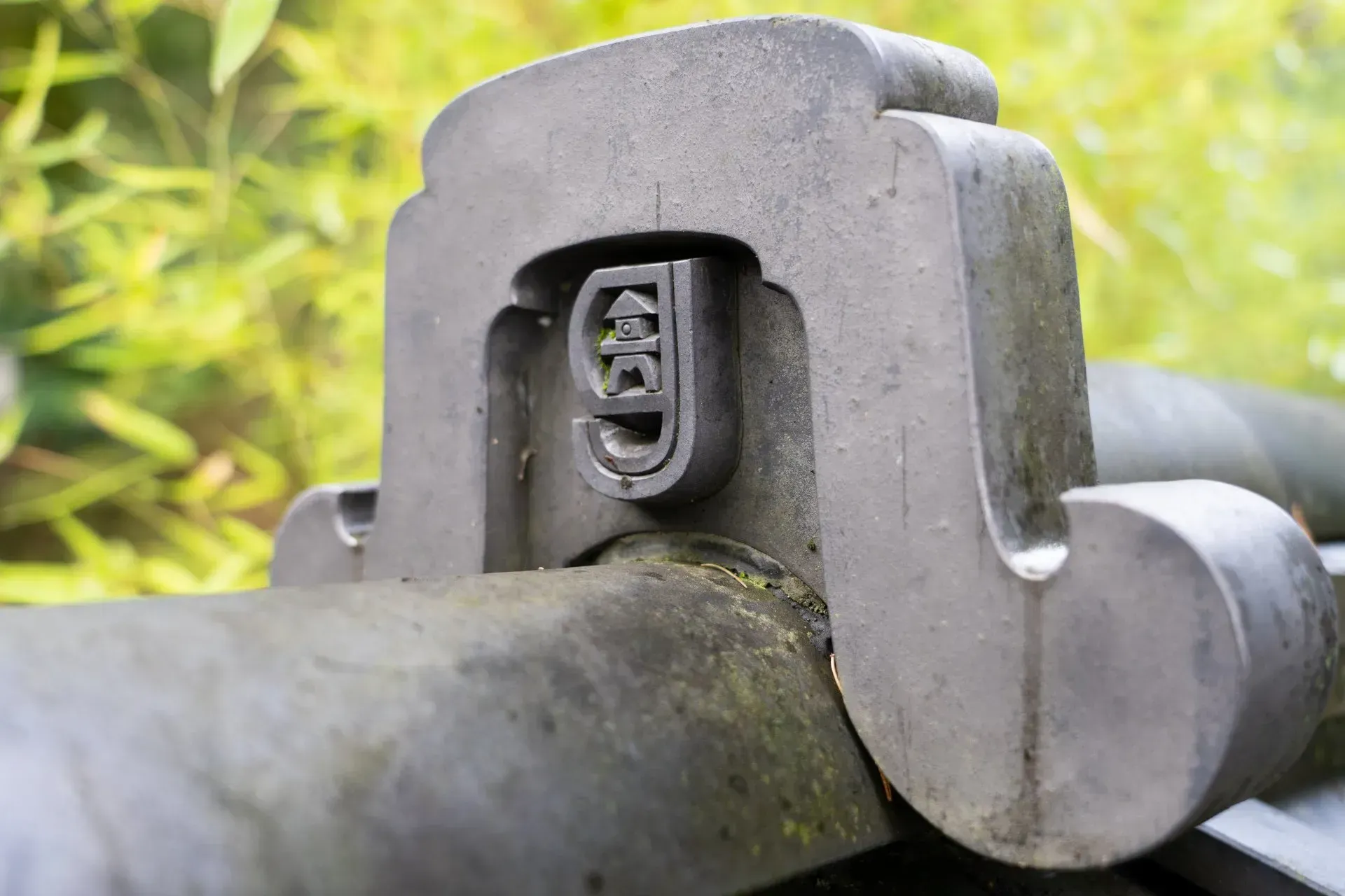Close-up of a metal decorative element with a stylized pagoda design, on a dark railing, blurred green background.