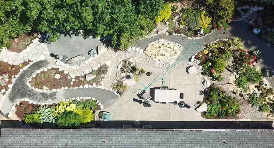 Overhead view of a landscaped backyard with winding paths, a patio table, and surrounding trees and bushes.