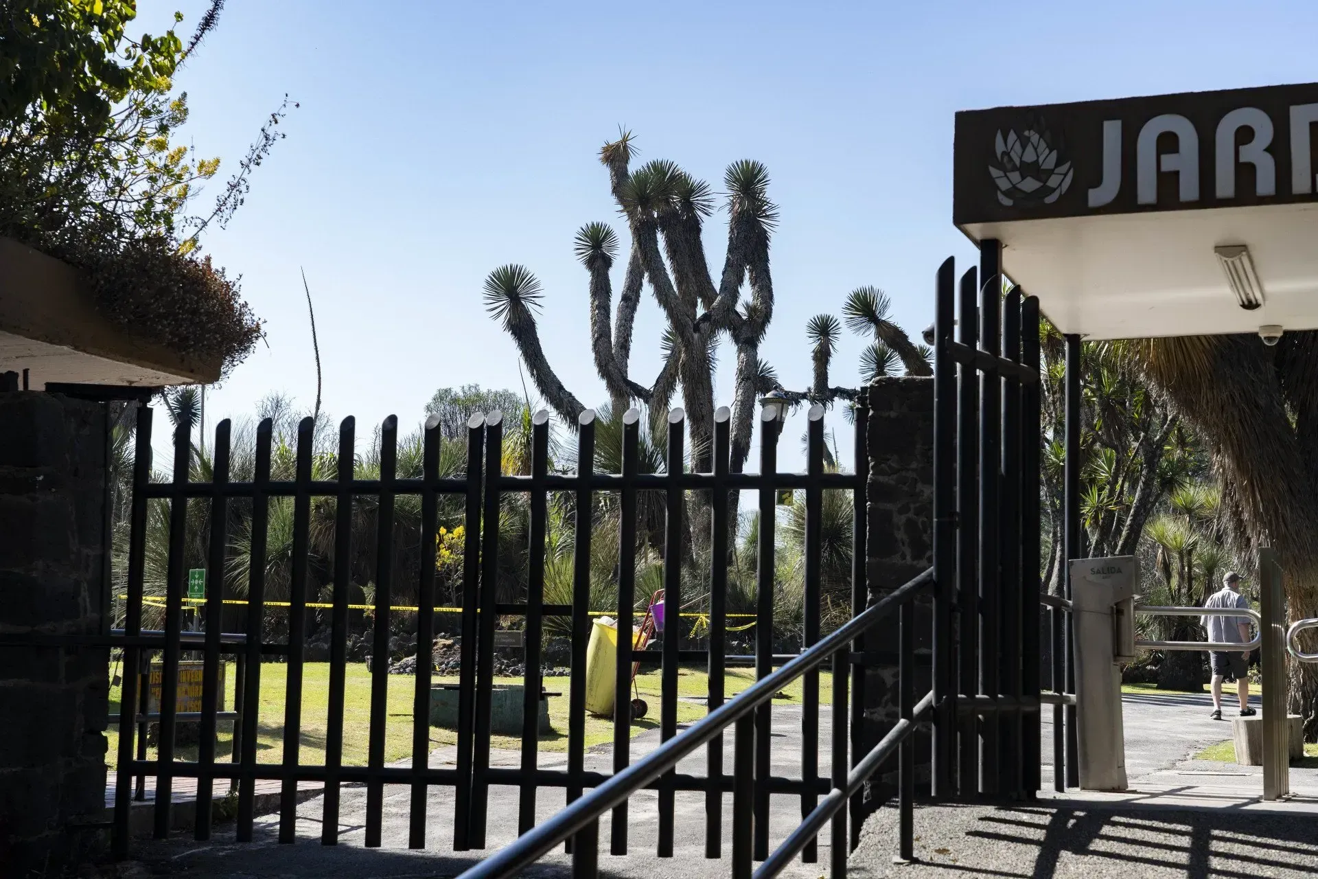 Black gate opening to a cemetery with headstones and green grass under a clear sky. The sign reads 