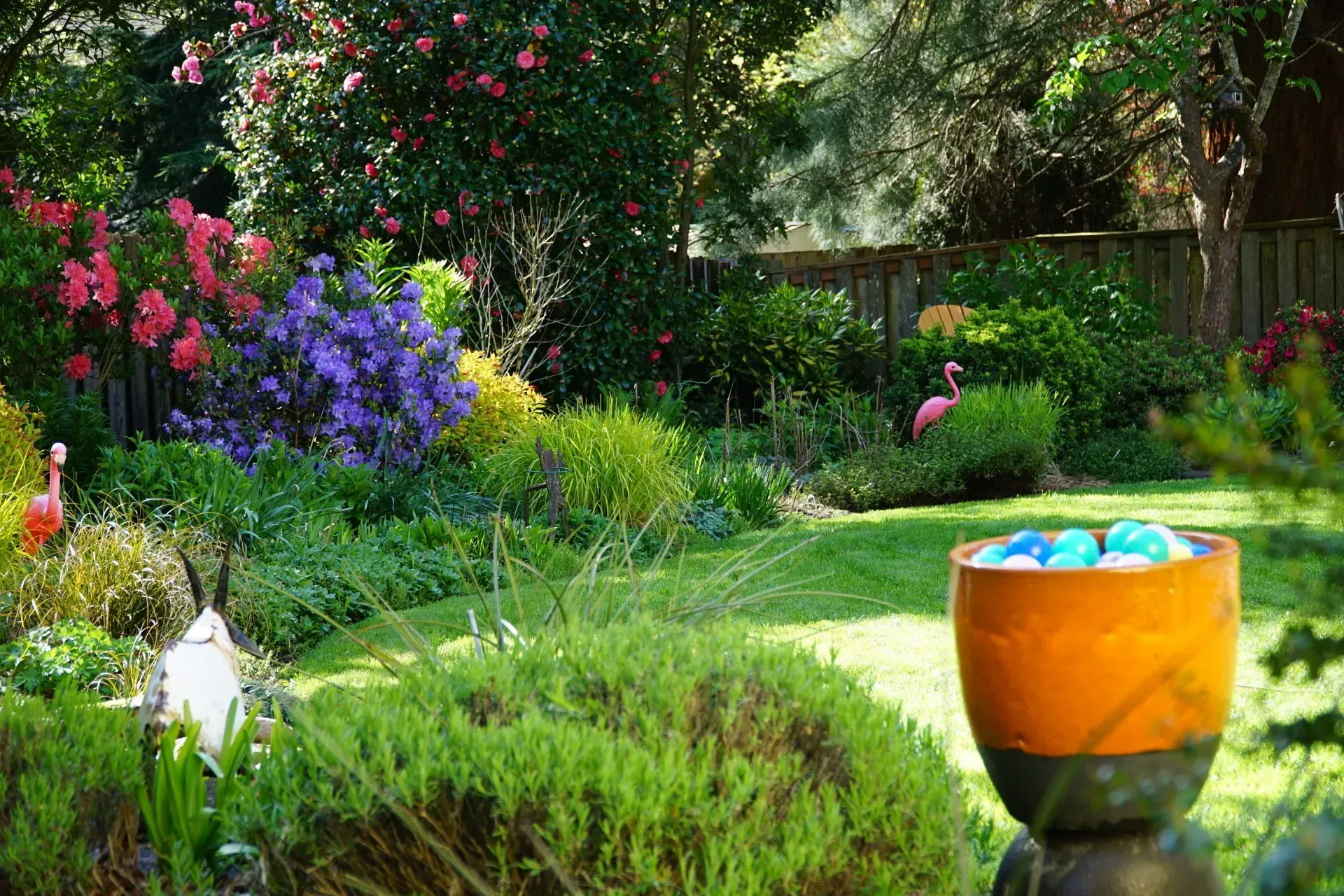A lush, colorful garden with blooming flowers, a grassy lawn, and decorative flamingos.
