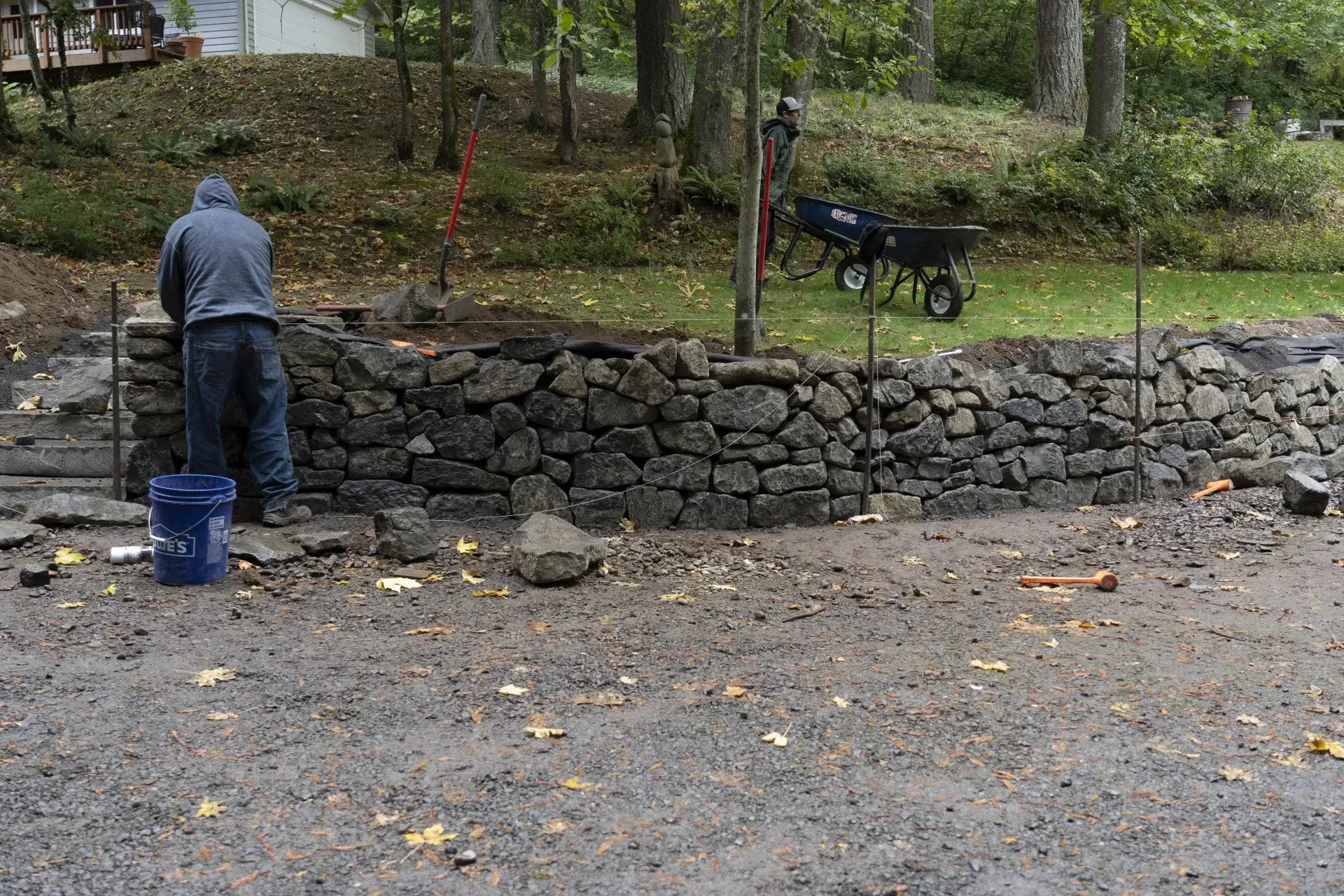 A person builds a stone wall outdoors on a wet day. 