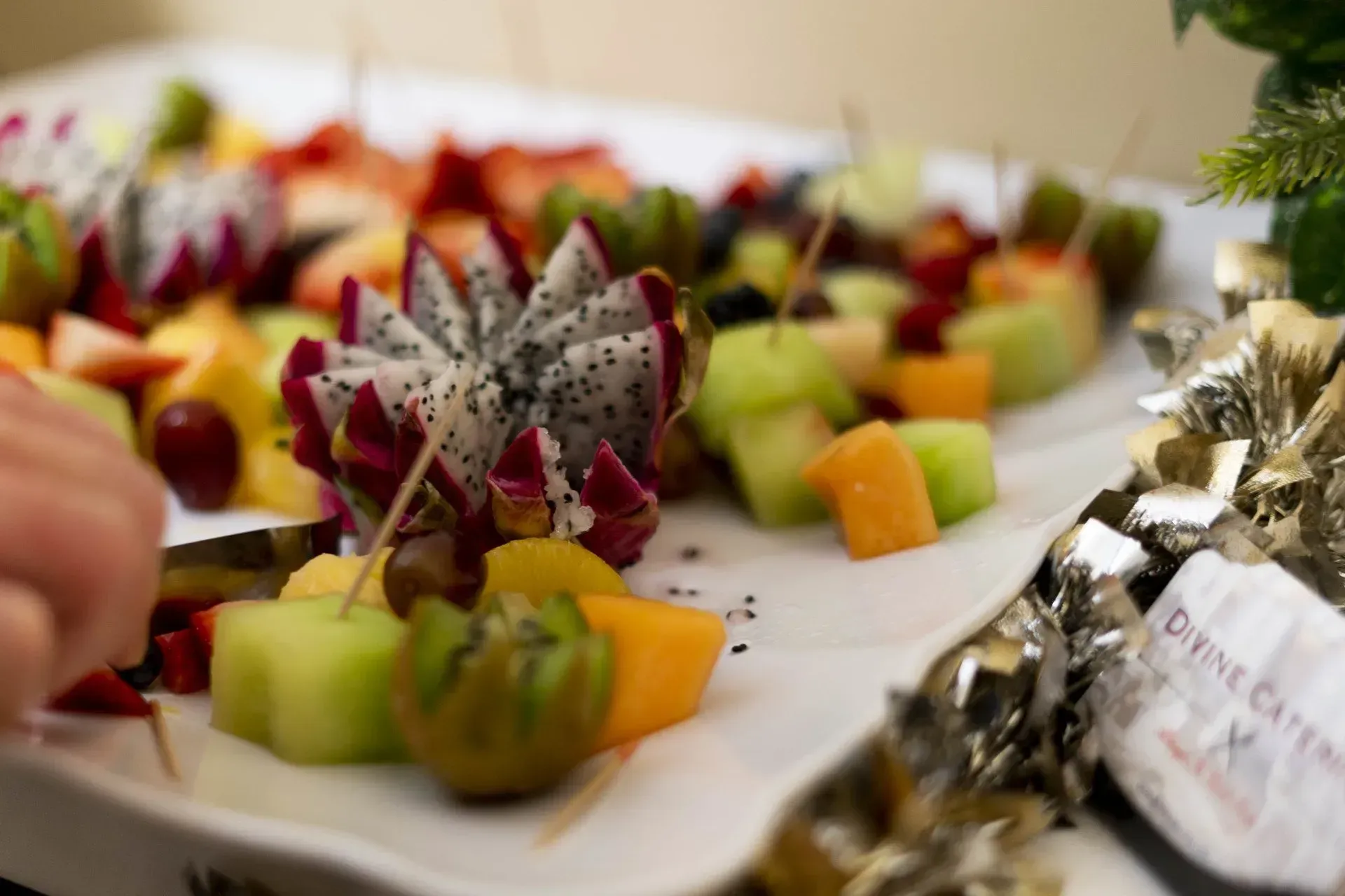 A white platter with assorted, colorful fruit skewers. Dragon fruit, cantaloupe, kiwi, and strawberries are featured.