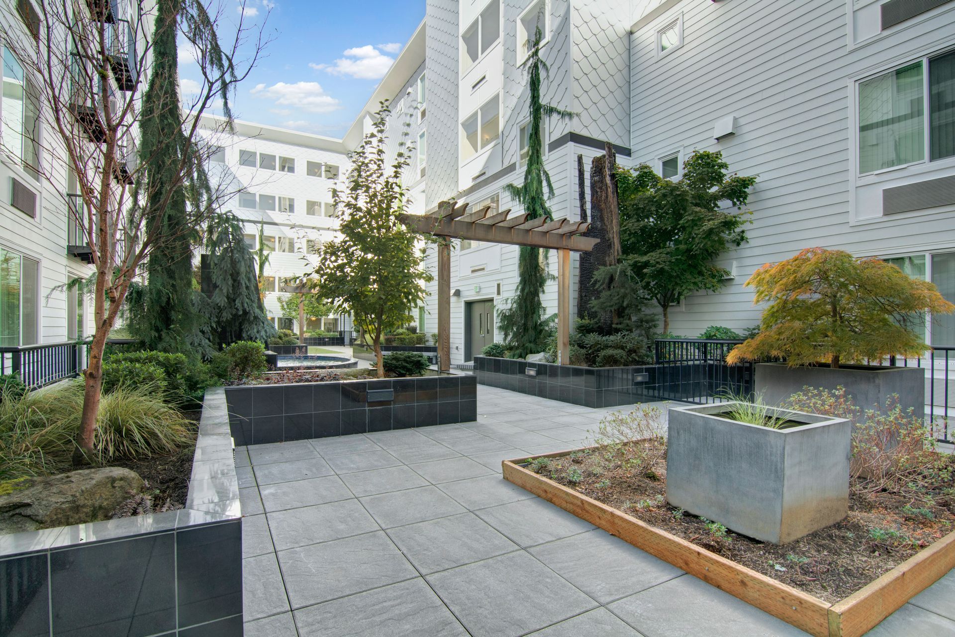 A courtyard with a pergola and planters in front of a building.