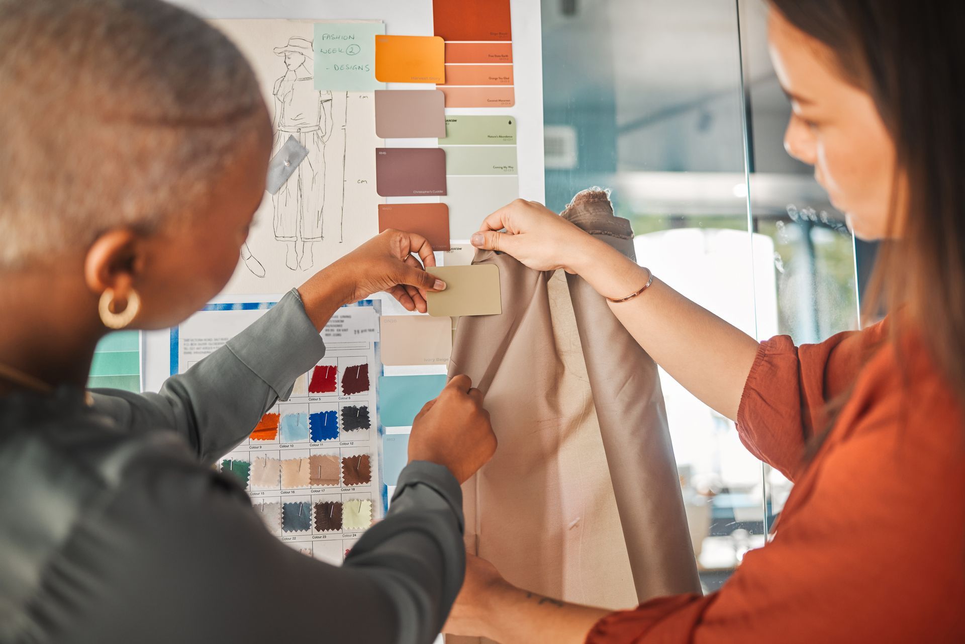 Two women choosing fabric samples with color swatches in a design studio.