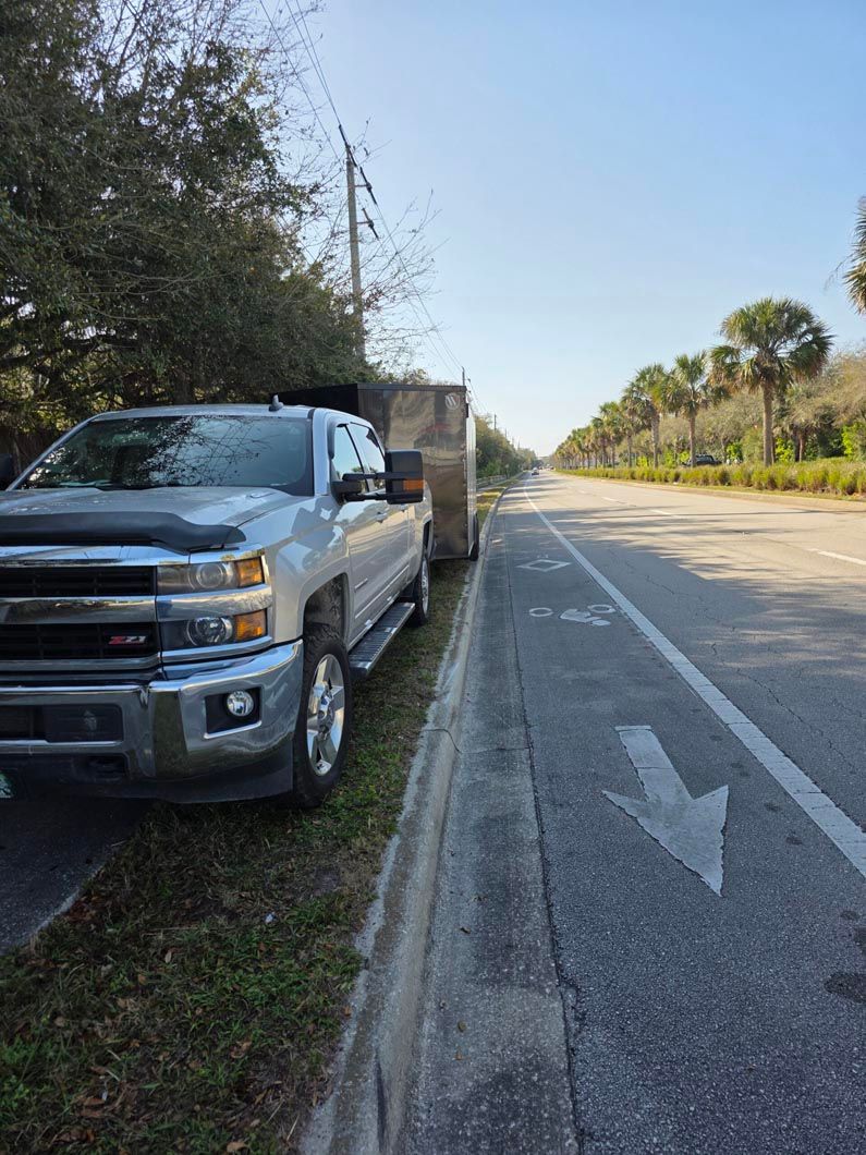 A silver truck is parked on the side of the road next to a trailer.