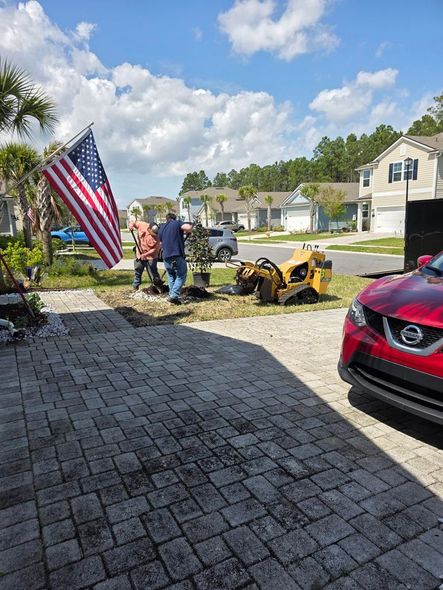 A red car is parked in a driveway next to a stump grinder.