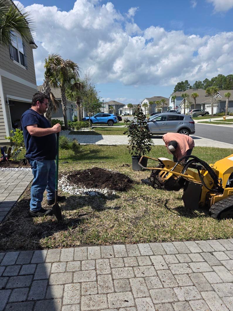 A man is standing next to a stump grinder in front of a house.