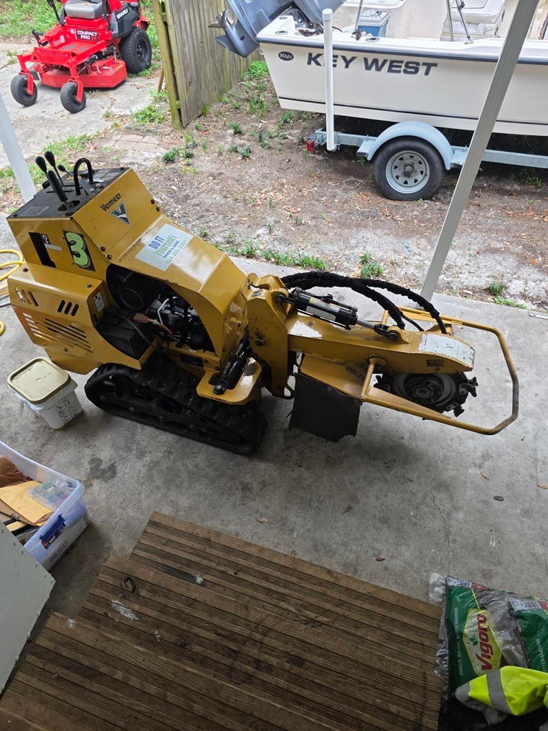 A yellow stump grinder is parked in a garage next to a boat.