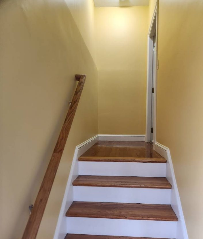Wooden staircase leading up to a doorway; yellow walls, white trim, wooden handrail.