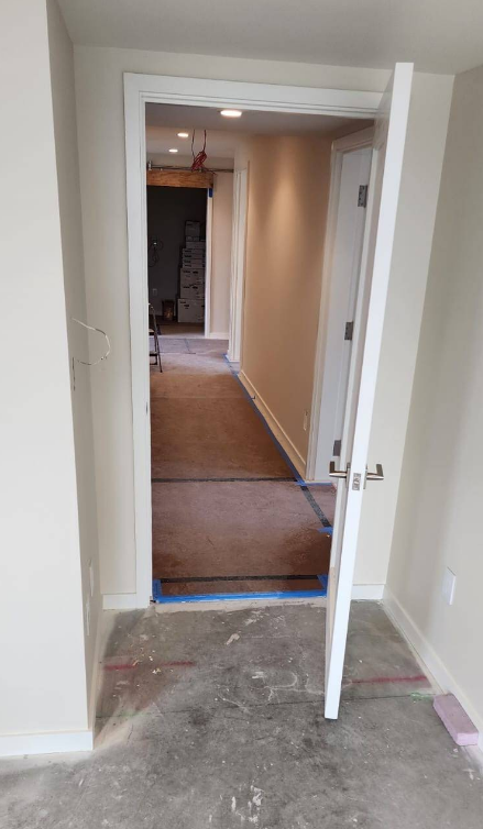 Open doorway into a hallway with a partially opened door on the right. Interior view with unfinished floor.