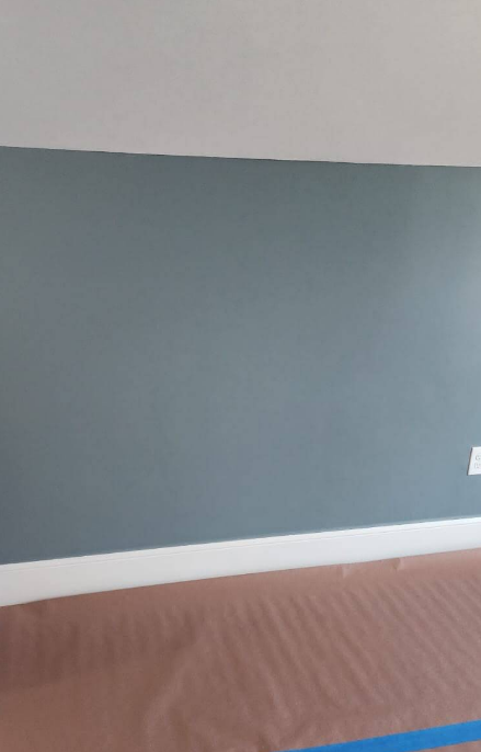 A room with a blue-gray painted wall, white trim, and a white ceiling. Brown paper covers the floor.