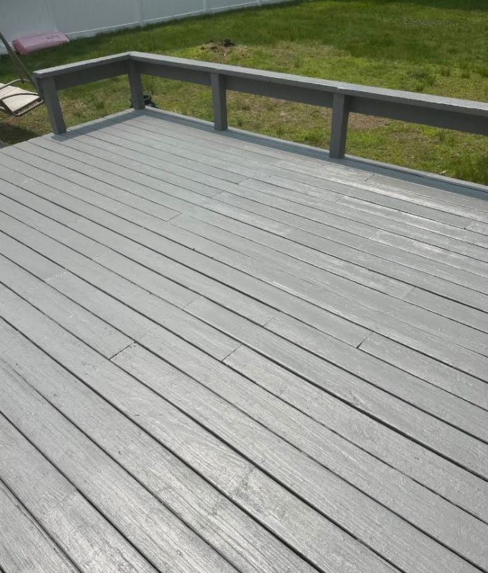 Gray composite deck with railings, overlooking a green lawn.