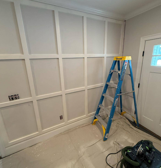White paneled wall with a blue ladder and a door on the right. Paint on the floor.