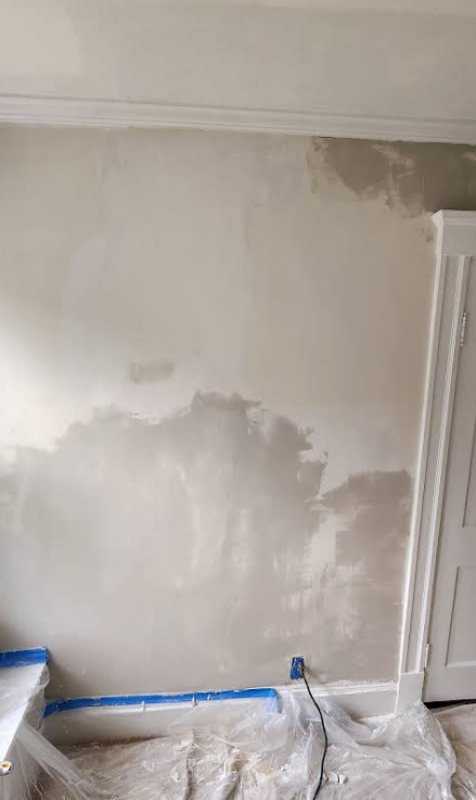 Wall with damp-looking patches. Light-colored paint, with lower portion appearing darker and stained. A doorway and baseboards are visible.