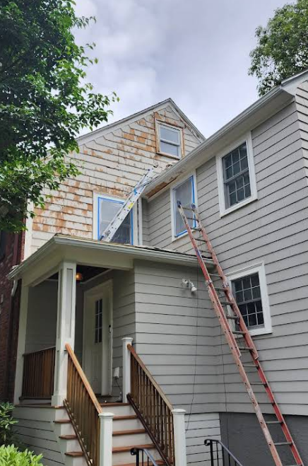 House exterior with ladders propped against the building, siding being painted.