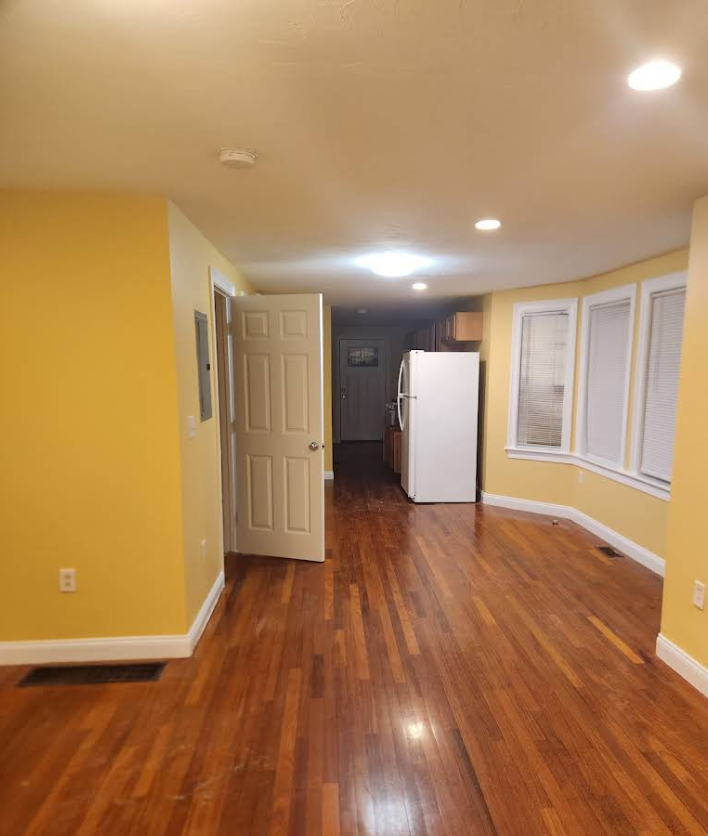 Open-concept living space with hardwood floors, yellow walls, and a white refrigerator in the kitchen.