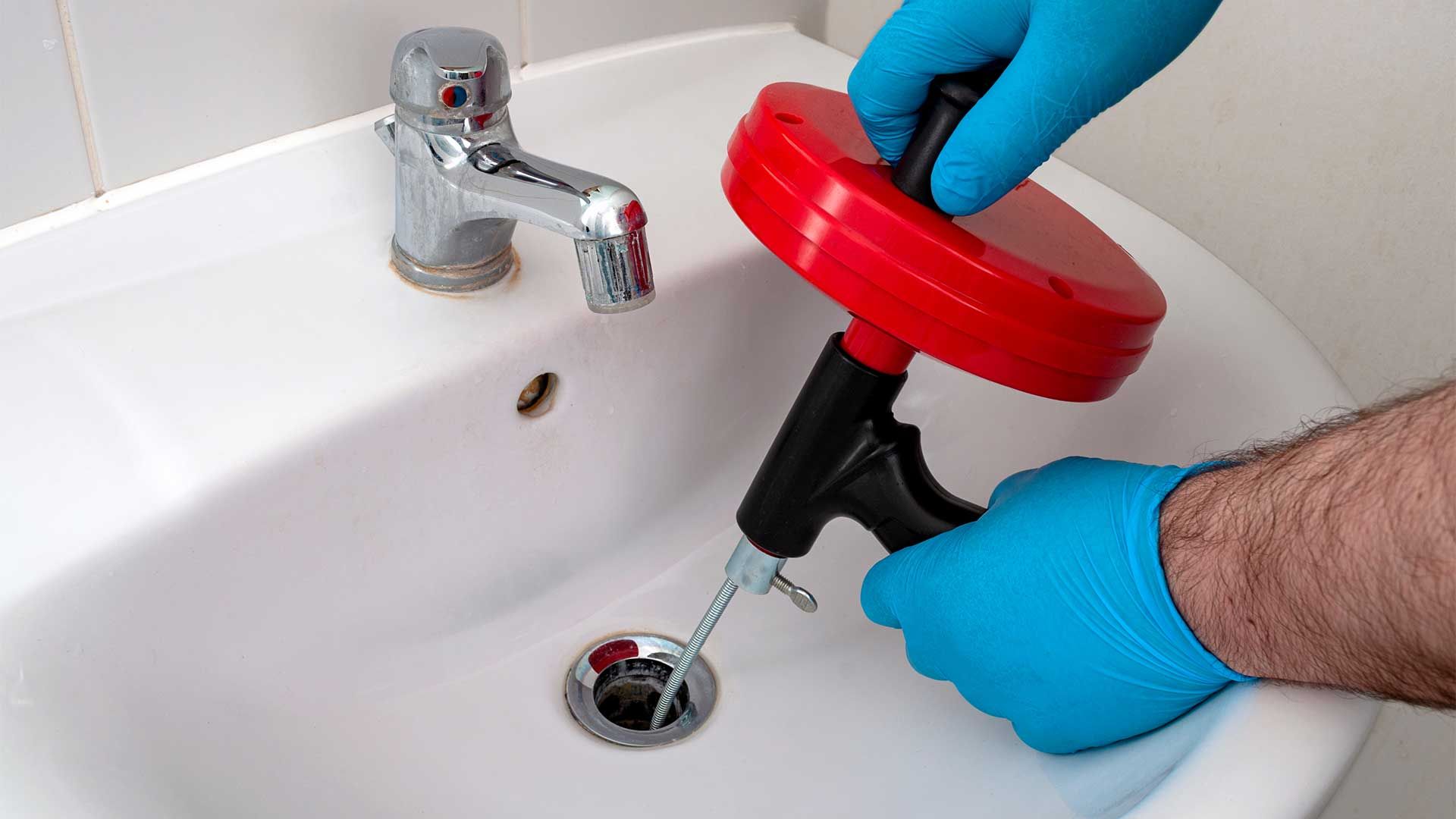 A person is using a drain snake to unblock a sink.
