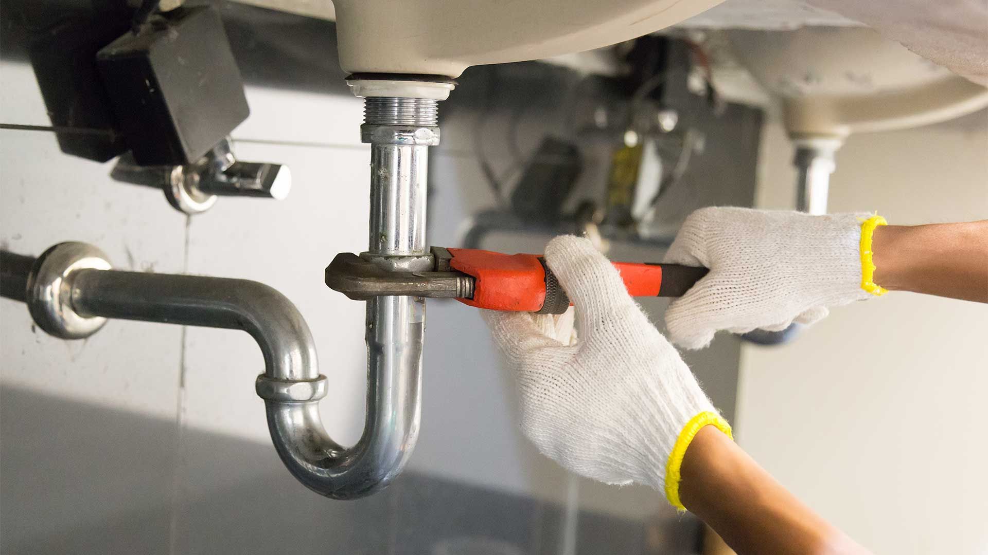 A plumber is fixing a sink pipe with a wrench.